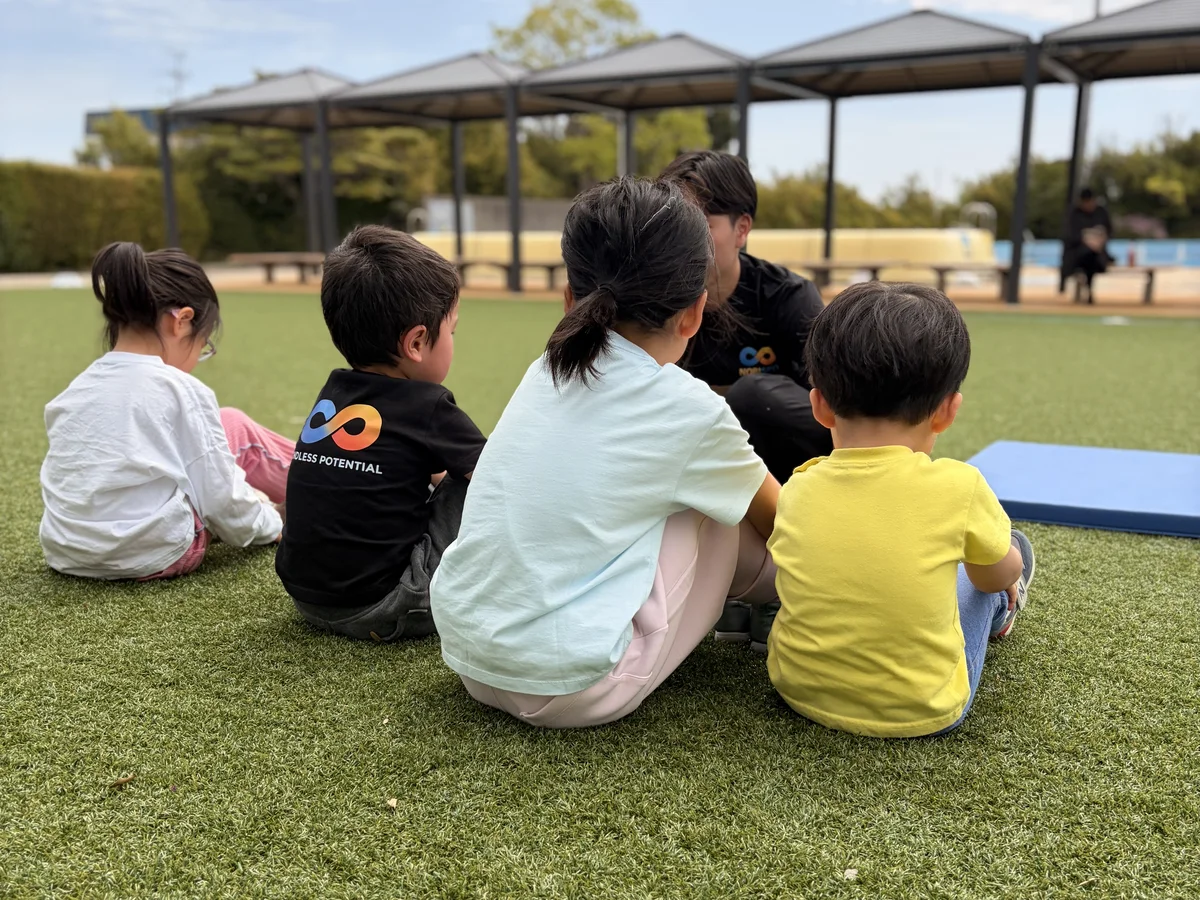 人工芝の会場でコーチを囲んで座る小学生クラスの子どもたち