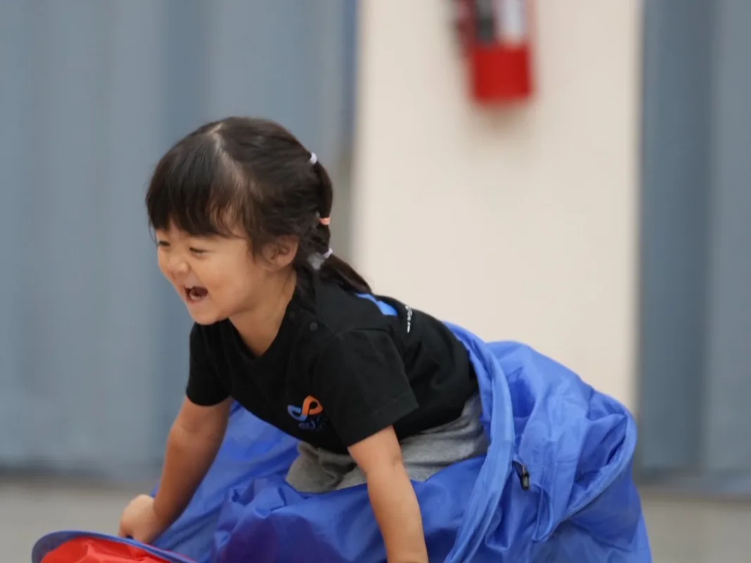 青いマットの上で笑いながら体を動かす2歳児