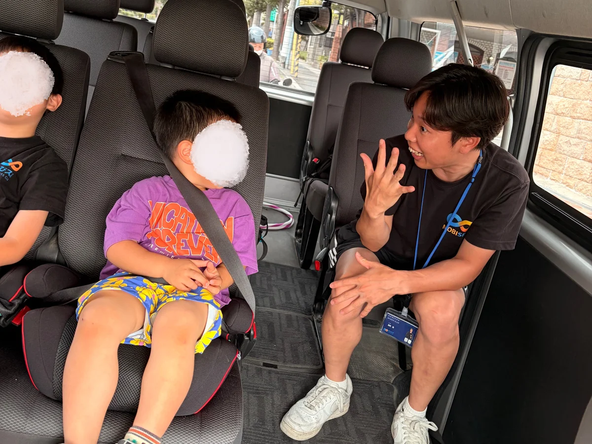 送迎中の車内でコーチが子どもたちと楽しそうに会話する様子