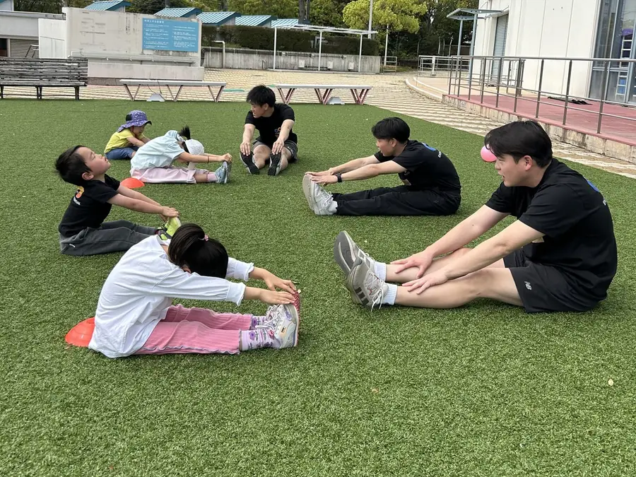 芦屋海浜公園 人工芝エリアでストレッチをする子どもたちとコーチ